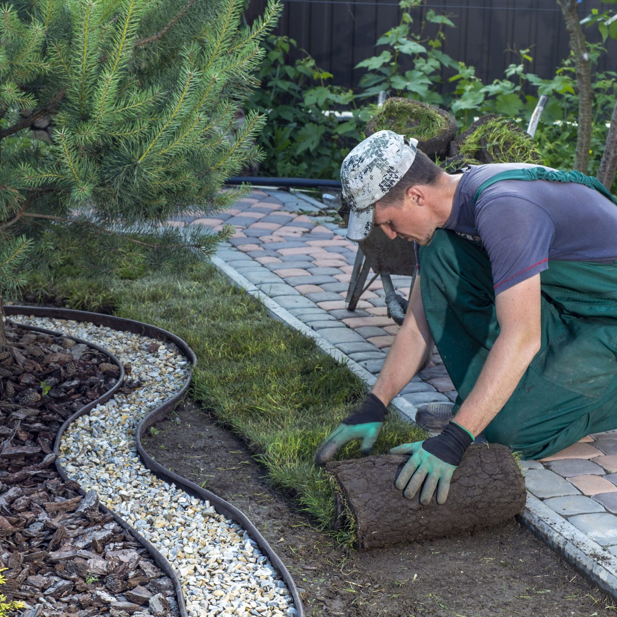 Landscape Gardener Laying Turf For New Lawn A man in green overalls and gloves kneeling down to work on the ground.